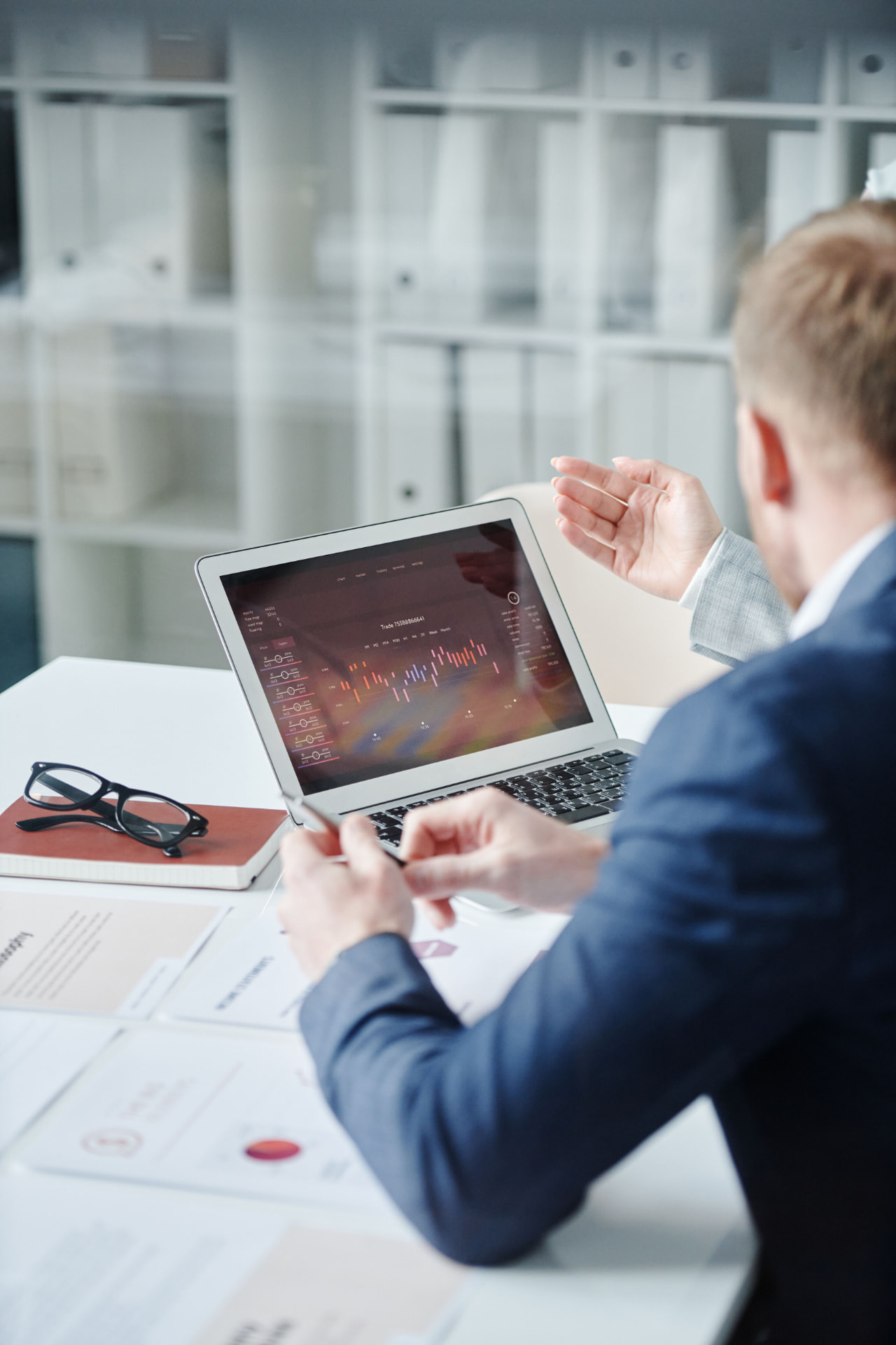 Profissionais analisando gráficos em um notebook e relatórios impressos durante uma reunião de gestão comercial e de marketing